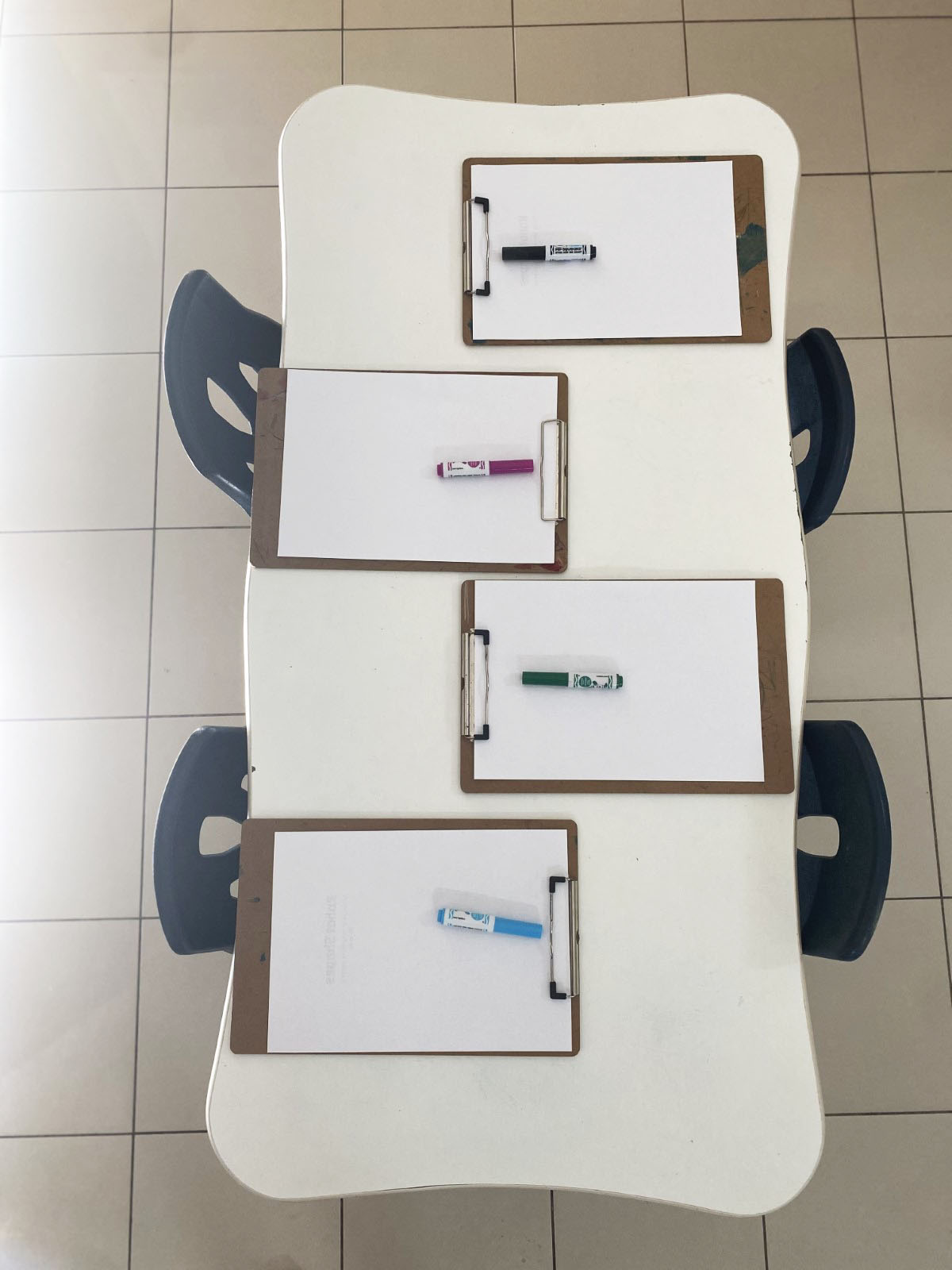 A low activity table set with four little chairs, each place laid with a clipboard of paper and a coloured marker ready for a drawing activity