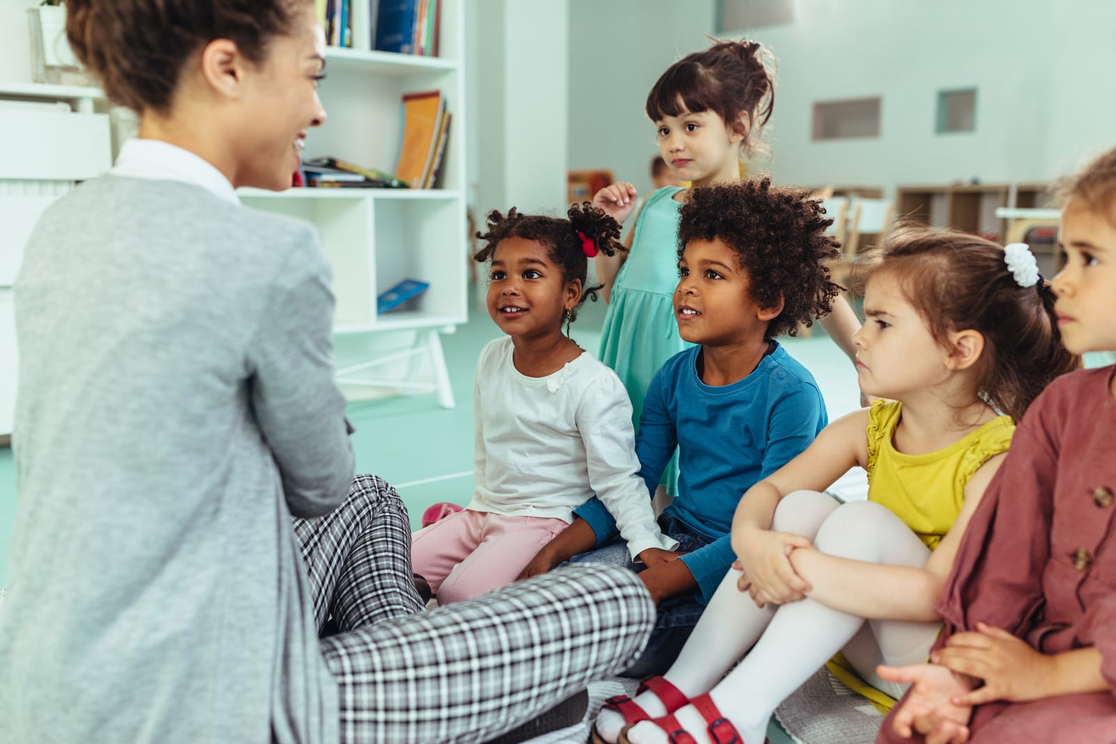 An early-learning educator sitting on the floor talking with a small, diverse group of young children during circle time