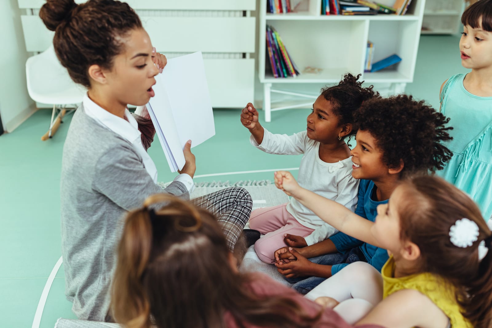 An educator reading a story to a circle of young children sitting together on the floor