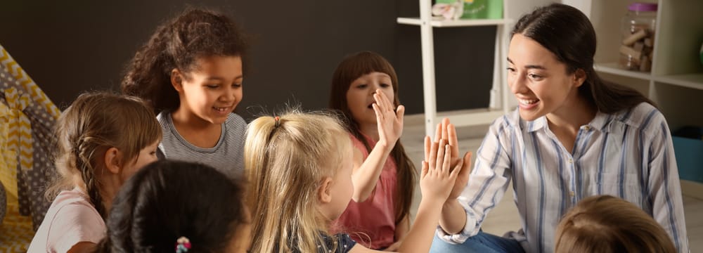 An educator and a group of smiling children sharing a high five together