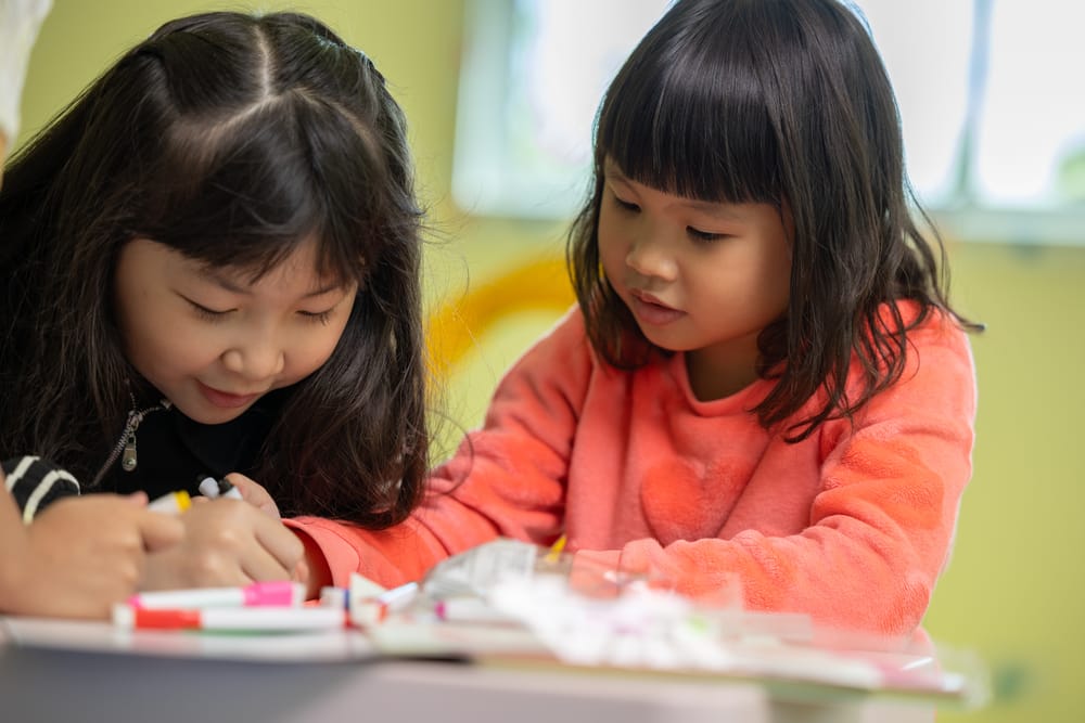 Two young children sitting close together, sharing a hands-on activity at a table