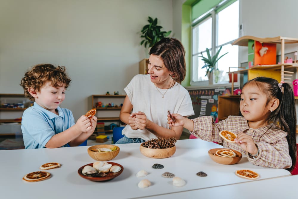 An educator and two children exploring a hands-on nature table of dried oranges, pine cones and shells